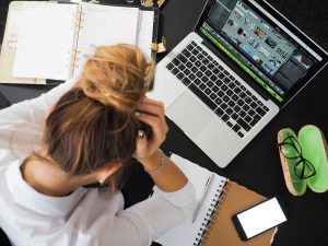 woman at cluttered work desk frustrated head down overwhelmed